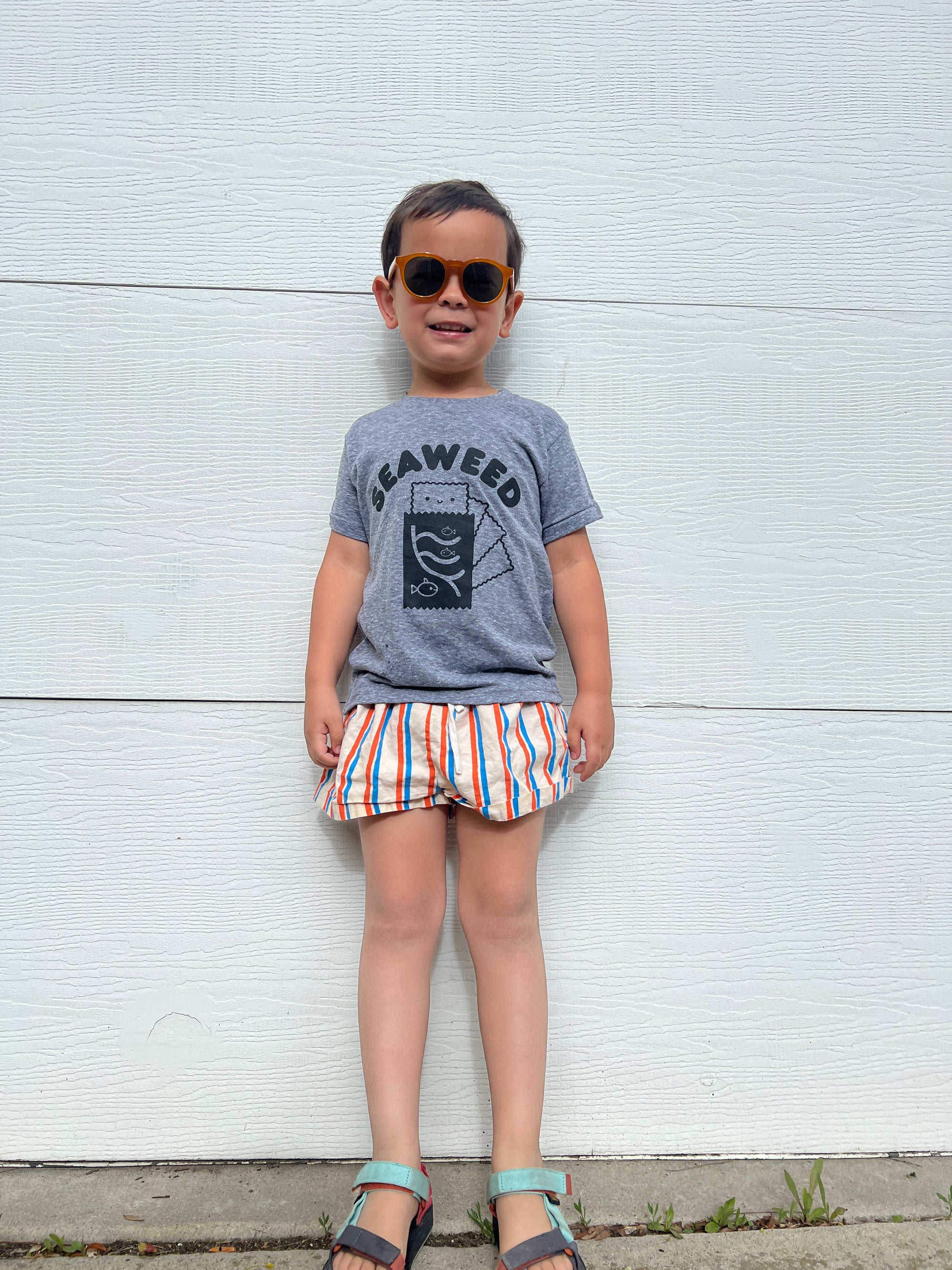 A child modeling a grey tee screen printed with black ink with text reading SEAWEED above a smiling package of seaweed.