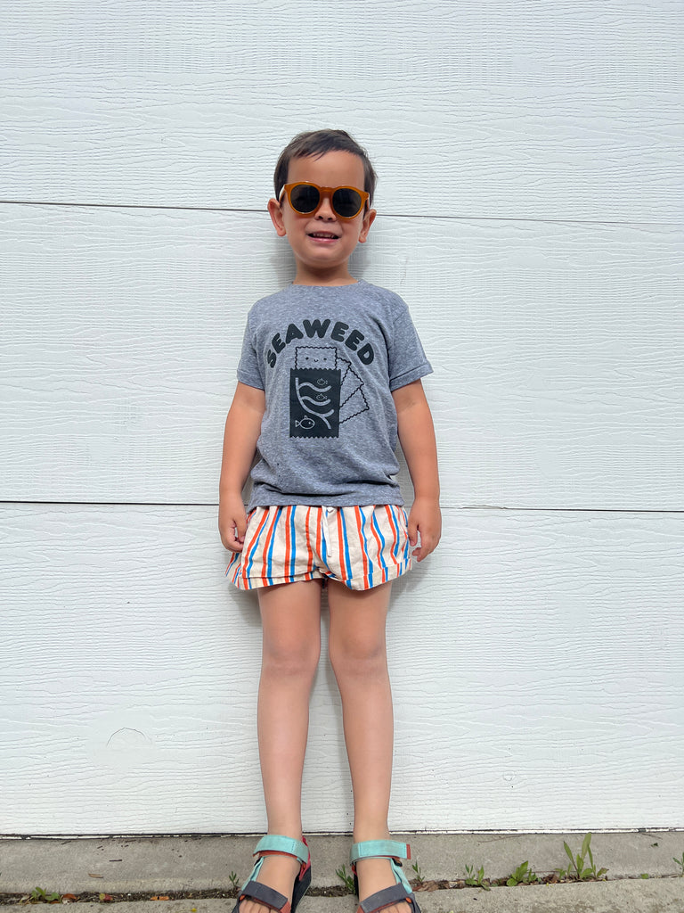 A child modeling a grey tee screen printed with black ink with text reading SEAWEED above a smiling package of seaweed.