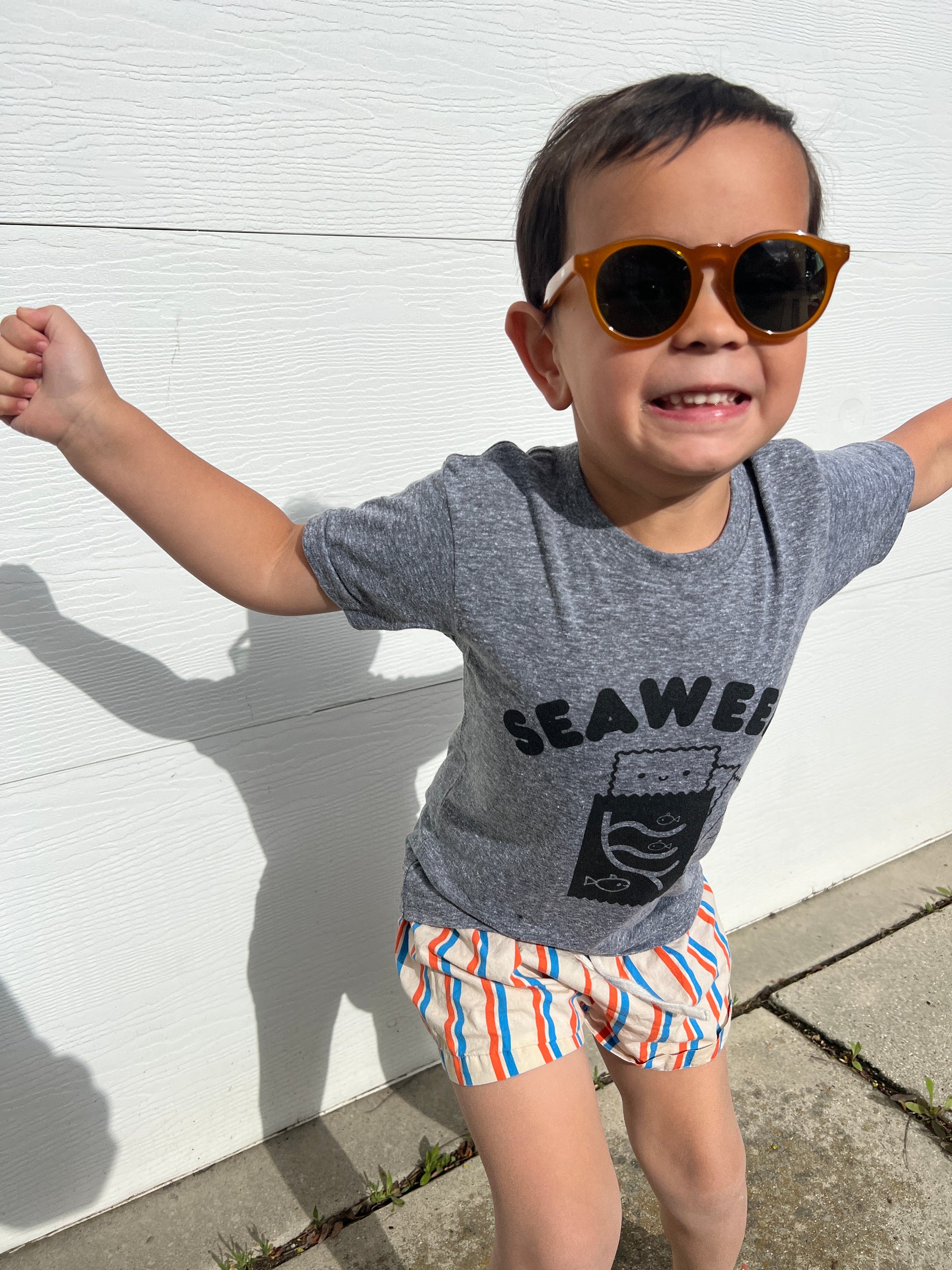 A child modeling a grey tee screen printed with black ink with text reading SEAWEED above a smiling package of seaweed.