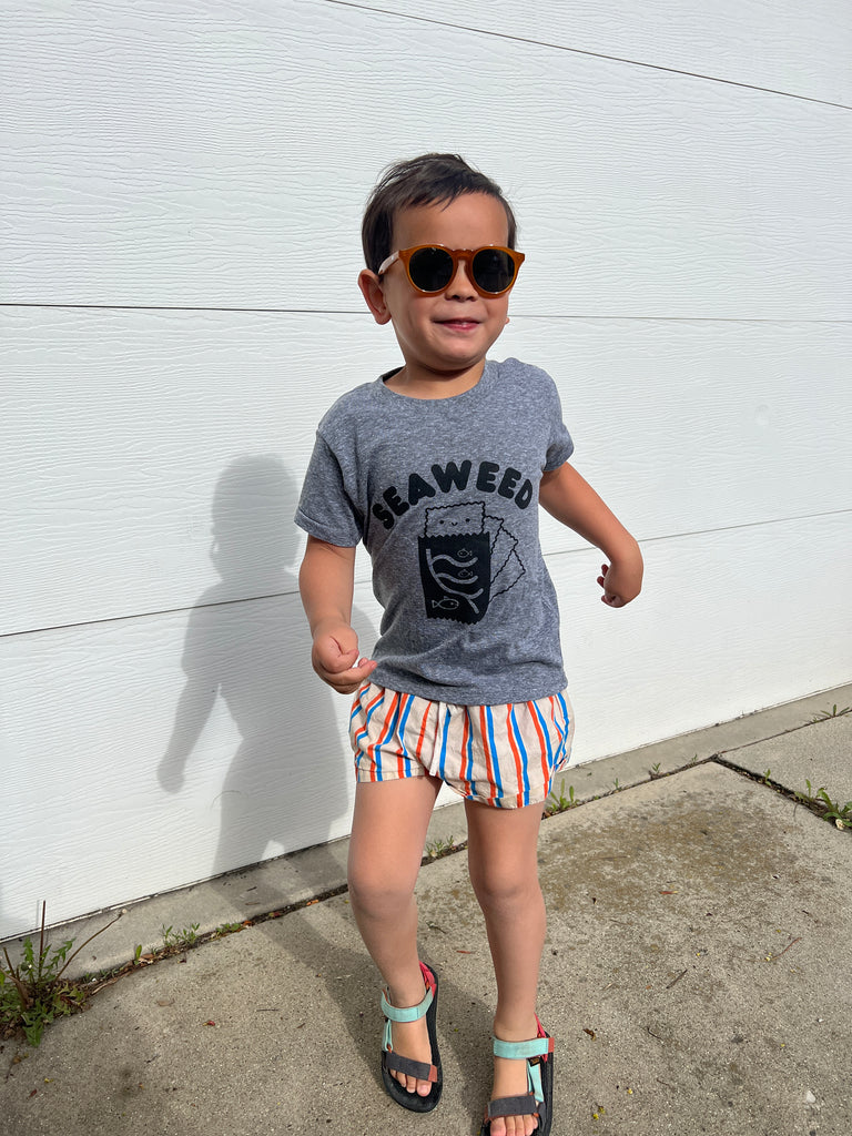 A child modeling a grey tee screen printed with black ink with text reading SEAWEED above a smiling package of seaweed.