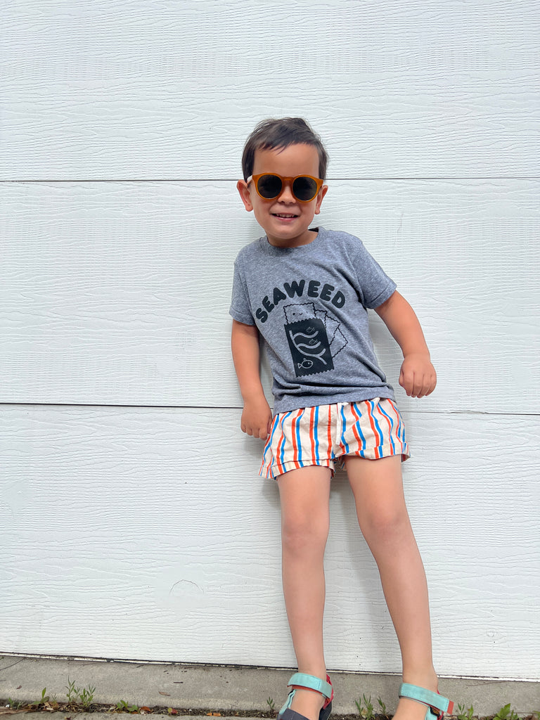 A child modeling a grey tee screen printed with black ink with text reading SEAWEED above a smiling package of seaweed.