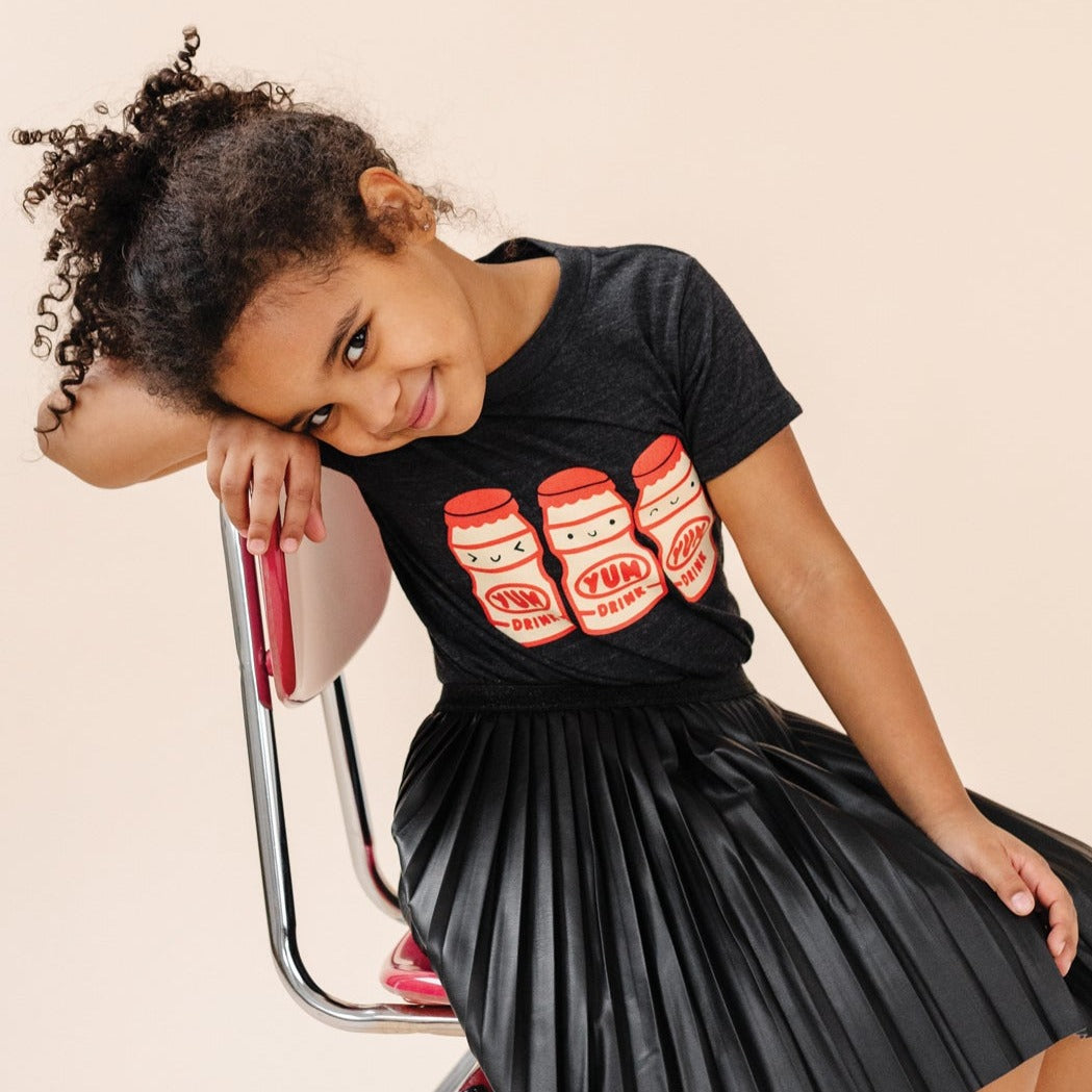 A child modeling a black tee screen printed with three red and yellow yakult yogurt bottles with smiley faces.