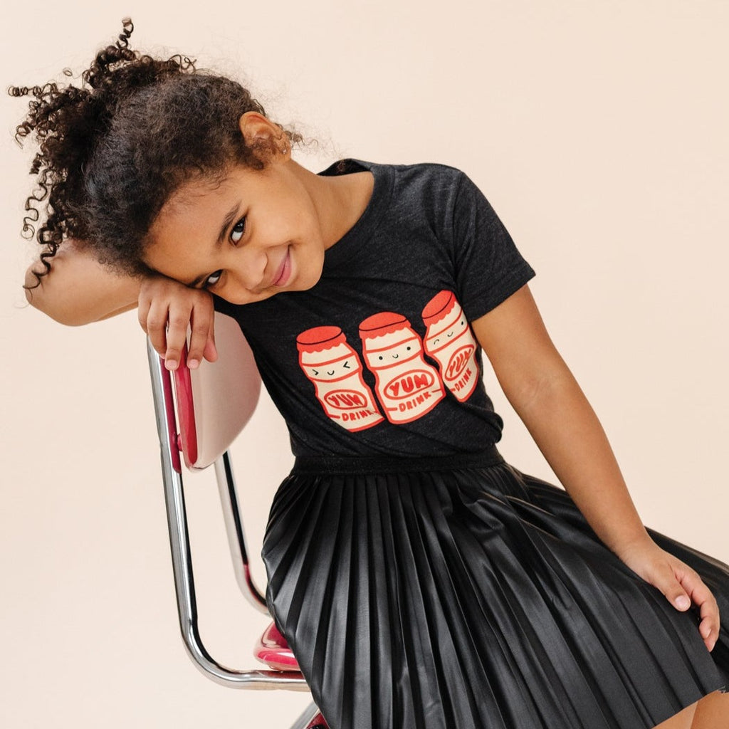 A child modeling a black tee screen printed with three red and yellow yakult yogurt bottles with smiley faces.