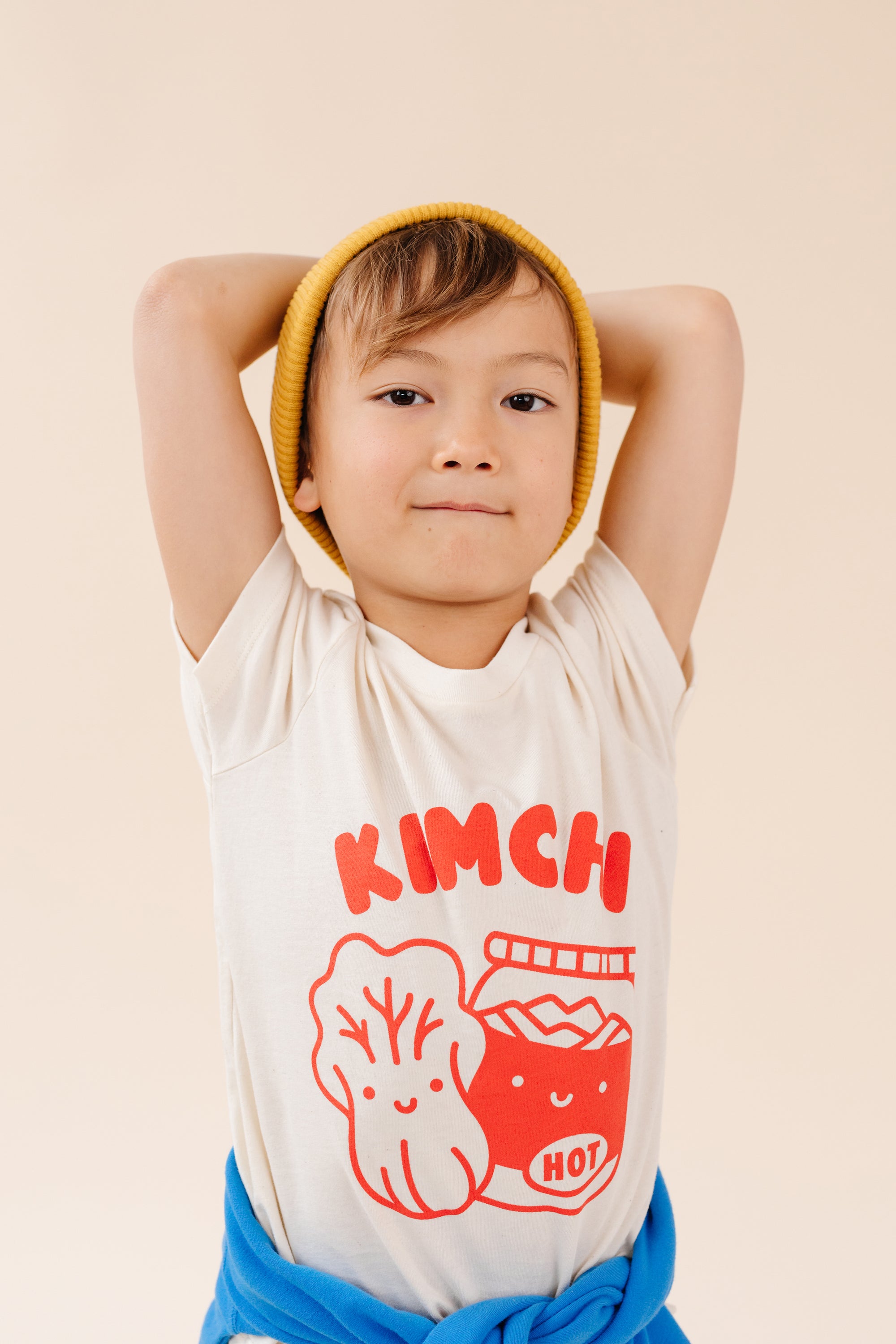 A child modeling a white tee screen printed with red ink, text KIMCHI and cabbage and jar of kimchi, both smiling.