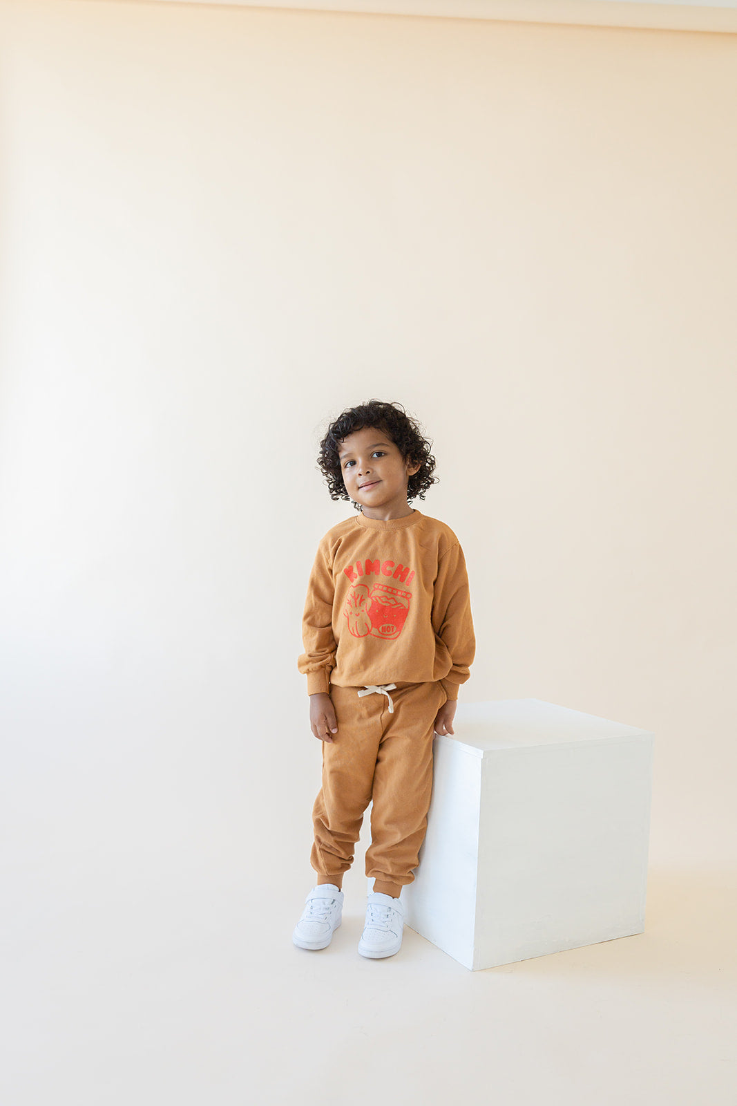 A child modeling brown sweatshirt screen printed with red ink, text KIMCHI and cabbage and jar of kimchi, both smiling.