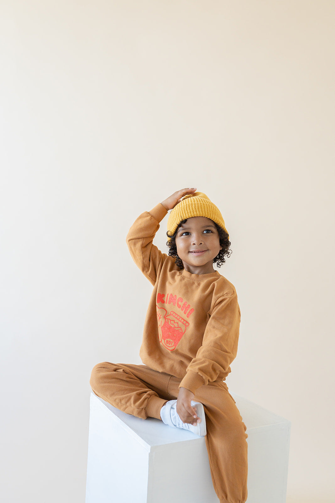 A child modeling brown sweatshirt screen printed with red ink, text KIMCHI and cabbage and jar of kimchi, both smiling.